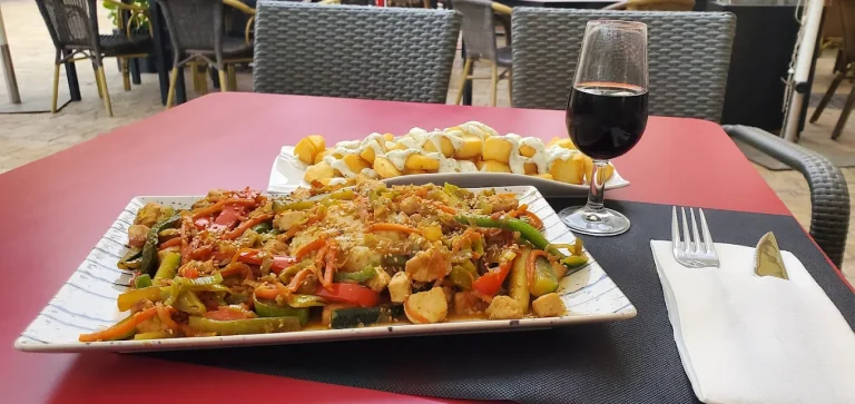 Plato de verduras salteadas con pollo, acompañado de un vaso de vino tinto y frituras.