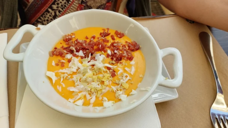 Crema de calabaza con trozos de bacon y queso rallado en un cuenco blanco.