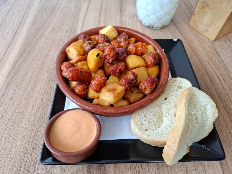 Papas a la brasa con salsa y pan en un plato negro sobre una mesa de madera.