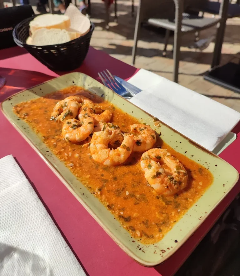 Gambas al ajillo en salsa sobre un plato, acompañadas de pan en un fondo exterior.
